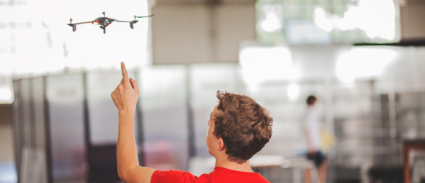 A young man pointing at a drone flying in front of him.