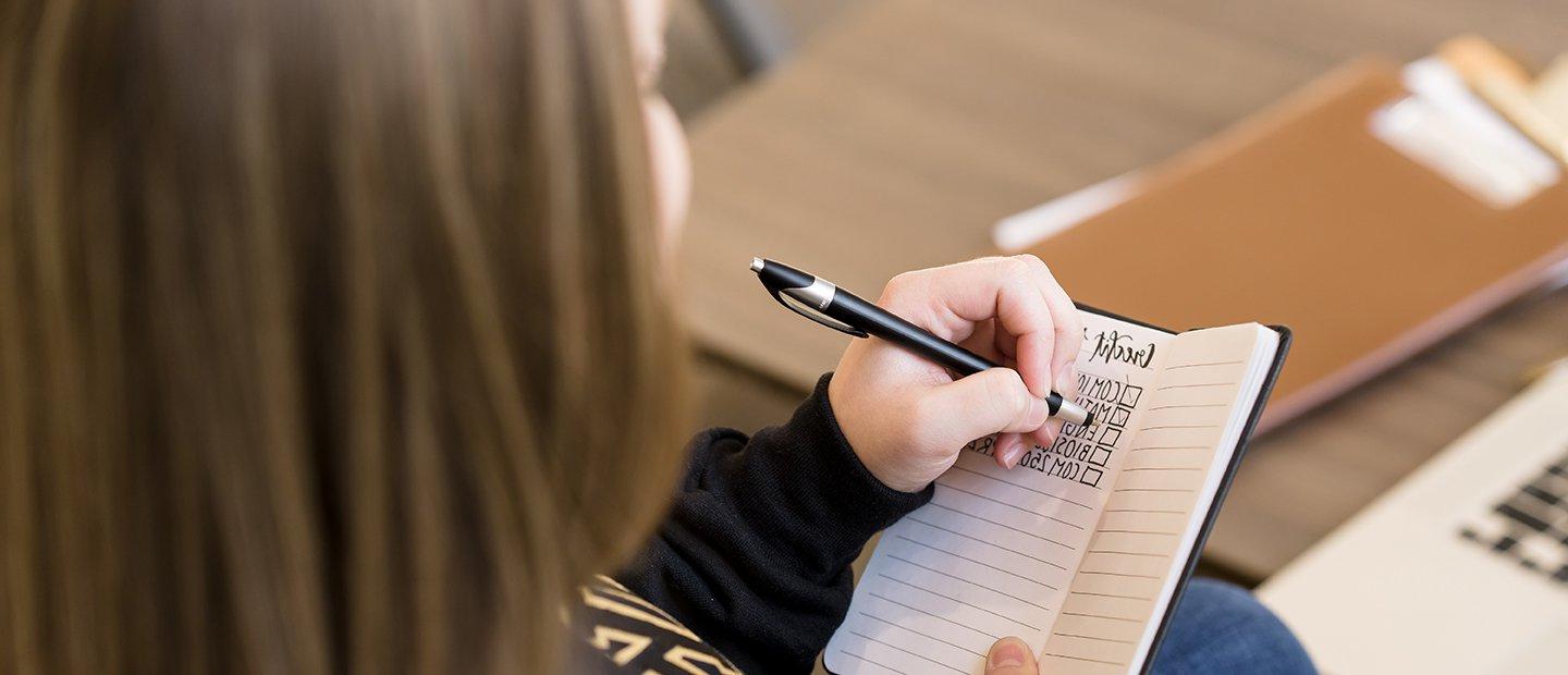 An Oakland University student making check marks next to courses listed in a notebook.